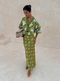Cardigan vert tricoté avec motifs d'yeux, boutons et manches surdimensionnées, associé à une jupe à motifs floraux assortie et des mules beiges à talons.
