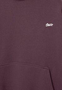 Sweat-shirt bordeaux avec une texture douce, doté d'une poche avant et d'un petit logo brodé blanc en haut à gauche.