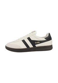 Zapatilla blanca con rayas negras y una puntera de ante. Presenta el logo de Gola en dorado en el lateral y una suela de goma oscura. Diseño atlético clásico.