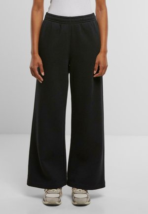 Czarne długie spodnie dresowe z szerokimi nogawkami i elastycznym pasem; miękka tkanina i gładka faktura. Noszone z neutralnymi sneakersami.