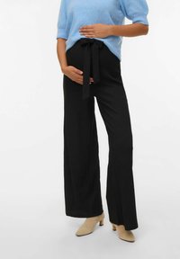 Črne široke hlače iz teksturirane tkanine z vezano elastiko. Ujemajo se z mehkimi modrimi majicami s kratkimi rokavi in bež čevlji na peto.