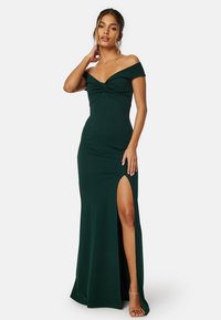 Abito verde scollato con busto aderente, dettaglio a torsione sul petto e uno spacco alto fino alla coscia. Realizzato in materiale liscio e elasticizzato.
