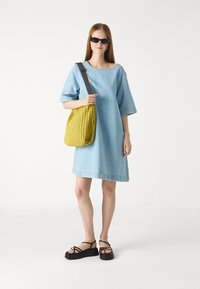 Robe chemise en denim bleu clair, à manches courtes, coupe ample. Comprend un sac plissé jaune avec une sangle foncée et des sandales à plateforme noires.