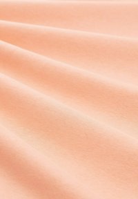 Brzoskwiniowa bawełniana tkanina o gładkiej fakturze, ukazująca delikatne fale i miękkie zgięcia, odpowiednia do różnych zastosowań tekstylnych.