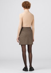 Beige geribde coltrui gecombineerd met een bruine minirok met patroon. Model draagt zwarte chunky schoenen en doorschijnende zwarte panty's.