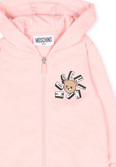 Jasnoróżowa bluza niemowlęca z kapturem, z zamkiem z przodu, metką Moschino wewnątrz kołnierza oraz grafiką misia i rozrzuconym napisem "MOSCHINO" na klatce piersiowej.