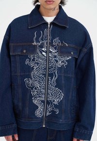 Jeansová bunda v tmavě modré barvě s vyšitým bílým drakem na přední straně, se zapínáním na zip a dvěma kapsami na hrudi.