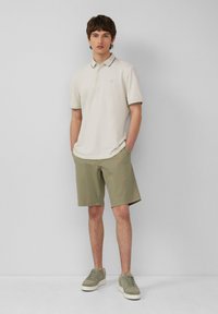 Beige poloshirt met een kraag met een donkere afwerking, gecombineerd met lichtgroene shorts. Grijze sneakers. Eenvoudig ontwerp, casual pasvorm.