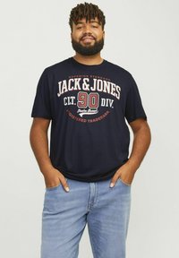 Marineblå bomulds T-shirt med hvid og rød grafisk tekst "JACK & JONES" og "90 DIV." på forsiden; korte ærmer, afslappet pasform, med denim jeans.