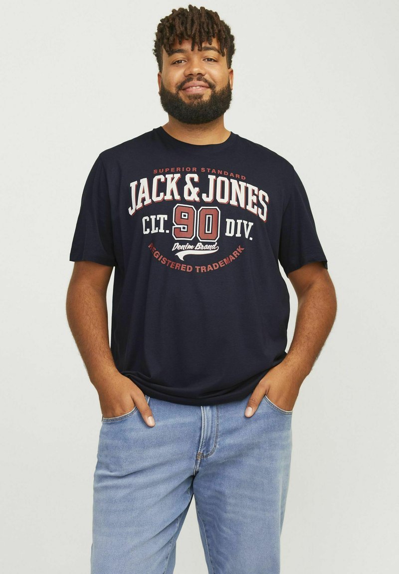 Marineblå bomulds T-shirt med hvid og rød grafisk tekst "JACK & JONES" og "90 DIV." på forsiden; korte ærmer, afslappet pasform, med denim jeans.