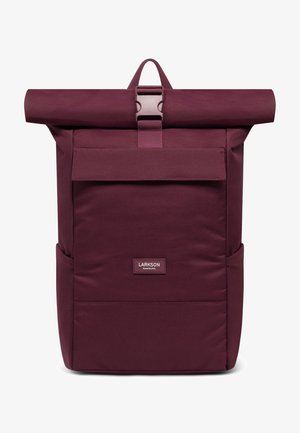 Mochila de color marrón con tapa enrollable, hecha de un tejido resistente, que cuenta con un bolsillo frontal, correa ajustable y un asa superior para facilitar el transporte.