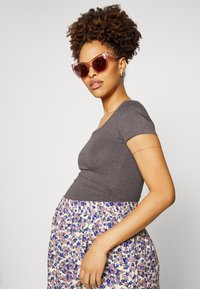 Top cinzento ajustado combinado com uma saia com padrão floral que apresenta detalhes em azul e roxo. Modelo usa óculos de sol oversized, cor-de-rosa.