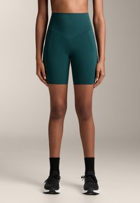 Korkeavyötäröiset, tummanvihreät pyöräilyshortsit, jotka on valmistettu joustavasta kankaasta, ja joissa on saumatön muotoilu sekä erottuvat sivupaneelit.