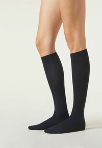 Knæhøje sokker lavet af et glat, strækbart stof i en ensfarvet mørk navy farve, med en ribbet kant og sømløst tådesign.