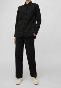 Černá košile na knoflíky s límečkem, dvěma náprsními kapsami a dlouhými rukávy, spárovaná s černými širokými kalhotami a krémovými teniskami.