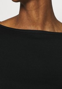 Top noir en tissu côtelé avec un décolleté décolleté. Texture de tissu douce. Vue rapprochée mettant en valeur son design sans couture et sa finition lisse.