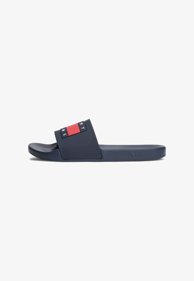 Marineblauwe slipper met rode en witte Tommy Jeans-logo op het bandje en geperst "JEANS" aan de zijkant van de zool.