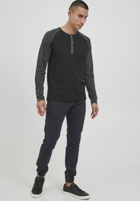 Long-sleeve black henley shirt with gray raglan sleeves, featuring a three-button placket. Paired with dark pants and black sneakers.