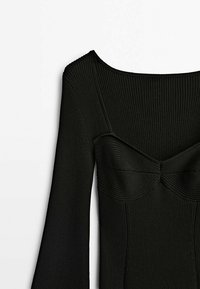 Bodysuit noir à côtes avec un décolleté large, un corsage structuré orné d'un nœud, et des manches longues. Tissu texturé avec des lignes verticales.