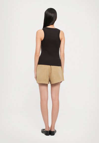 Black ribbed tank top paired with beige shorts, featuring back pockets. Model has straight hair and black flats. Plain white background.