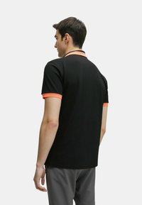 Polo shirt nera realizzata in tessuto morbido, con colletto e maniche in arancione, taglio classico e maniche corte.