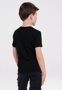 Black short-sleeve t-shirt with a crew neckline, made of smooth fabric, worn with dark pants. View shows back of the shirt.