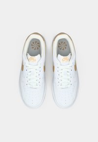 Białe skórzane trampki Nike Air Force 1 z złotymi akcentami, płaskimi sznurówkami, perforowanym noskiem oraz markowym językiem i wkładką.