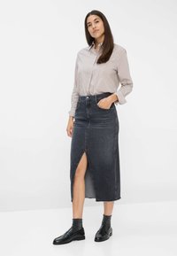 Denimskørt med en frontslids, falmet mørk vask og flagrende kant. Kombineret med en stripet skjorte med knapper og sorte loafers.