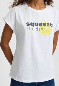 Valge puuvillane t-särk lühikeste varrukatega, millel on musta värvi "squeeze the day" tekst ja ees kollase sidruni graafika.