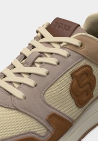 Καθημερινό αθλητικό παπούτσι με μπεζ ύφασμα, ταμπά σουέντ επενδύσεις, κρεμ κορδόνια και καφέ δερμάτινες λεπτομέρειες, συμπεριλαμβανομένου ανάγλυφου λογότυπου "BOSS" στη γλώσσα και την πλευρά.