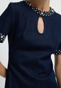 Robe en denim marine avec des manches courtes ornées de cristaux, un décolleté clé, et une texture lisse, mettant en valeur des clous décoratifs sur les bords.