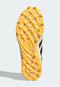 Sko sulan har ett texturerat gult gummimönster med diamantmönster och ett svart streck längs sidan, märkt med "adidas."