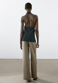Černý tílkový top s otevřenými zády, v kombinaci se světle hnědými kalhotami s širokými nohavicemi a jemným vertikálním proužkováním. Hladká textura látky.