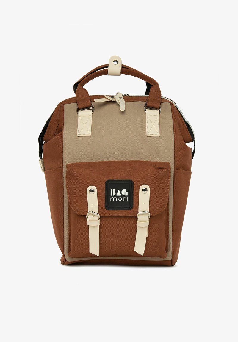 Sac à dos en tissu marron et beige avec des sangles réglables, une poignée supérieure, une poche avant avec rabat et des accents métalliques blancs. Logo sur le devant.