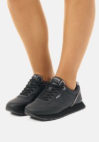 Schwarze Sportschuhe mit strukturiertem Obermaterial aus synthetischem Material, runder Zehenpartie und schnürbarem Verschluss. Verfügt über silberne Akzente und eine gepolsterte Sohle.