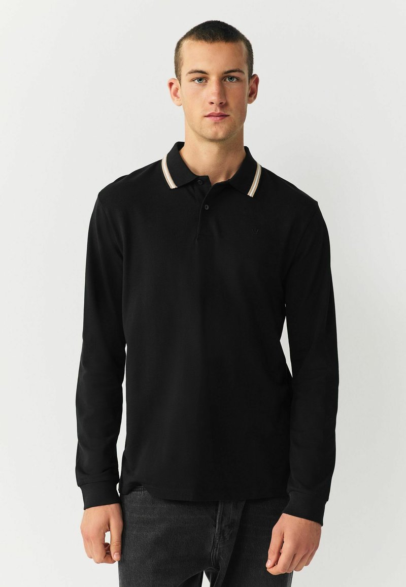 Schwarzes langärmeliges Poloshirt mit einem kontrastierenden gestreiften Kragen. Der Stoff hat eine glatte Textur und zeigt ein dezentes Logo auf der Brust.