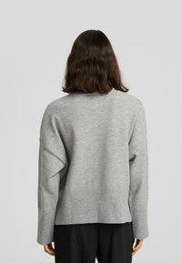 Szary, oversize sweter z prążkowanym dołem i mankietami, o miękkiej teksturze i opadających ramionach. Widok z tyłu pokazujący minimalne detale.