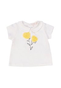 Camicia bianca in cotone a maniche corte con colletto Peter Pan, caratterizzata da tre fiori a pom-pom gialli e un'illustrazione di foglia nera sottostante.