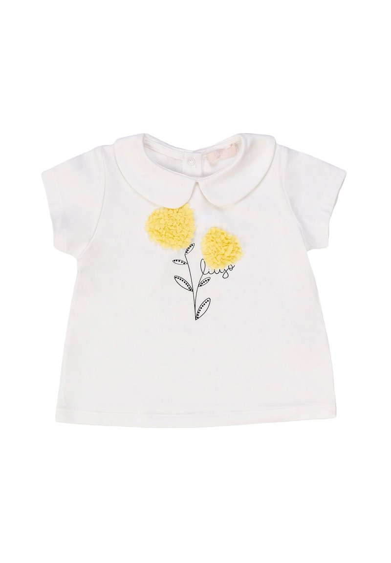 Camicia bianca in cotone a maniche corte con colletto Peter Pan, caratterizzata da tre fiori a pom-pom gialli e un'illustrazione di foglia nera sottostante.