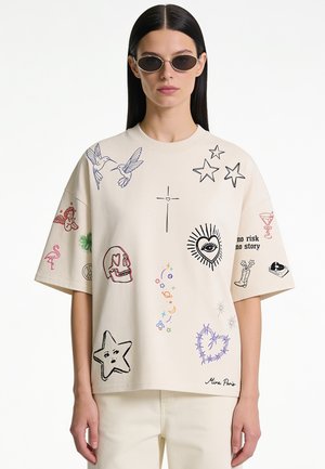Vrouw draagt een off-white oversized T-shirt met kleurrijke krabbels waaronder vogels, sterren, schedel, hart, oog en tekst "no risk no story" en een zonnebril.