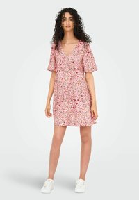 Ziedu kleita ar rozā fonu, kurā ir mazi daudzkrāsu ziedi, V veida dekoltē, īsām piedurknēm un brīvu piegriezumu. Tā valkāta ar baltām sporta kurpēm.