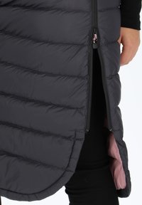 Puffer-väst i mörkgrått med quiltat mönster, med dragkedja och en kontrasterande rosa foder som syns från fållen.