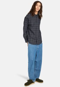 Navy button-up skjorte med et rutet mønster, parret med løstsiddende lyseblå jeans og mørkegrønne sko. Lange ærmer, afslappet design.