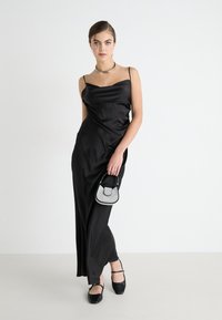 Schwarzes Satin-Abendkleid mit tailliertem Oberteil und schwingendem Rock, kombiniert mit einer kleinen metallischen Handtasche und schwarzen flachen Schuhen.