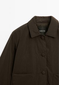 Veste marron avec un devant à boutons, un large col et deux poches avant. Fabriquée en tissu texturé avec une finition lisse.