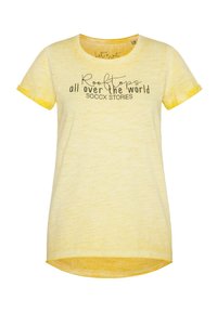 Gelbes T-Shirt mit kurzen Ärmeln und rundem Ausschnitt. Auf der Vorderseite befindet sich der schwarze Text "Dächer auf der ganzen Welt SOCCX GESCHICHTEN". Weicher Stoff.