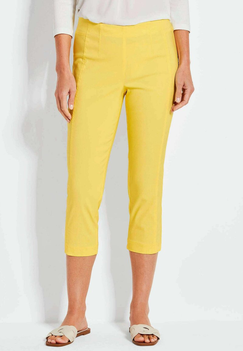 Gele cropped broek gemaakt van gladde stof, met een aansluitende taille en zijzakken. Draag met lichtgekleurde platte sandalen.