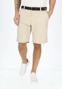 Beige shorts dengan potongan lurus, dilengkapi dengan hem jahitan, saku samping, dan sabuk anyaman biru navy. Dipadukan dengan sepatu sneaker putih.