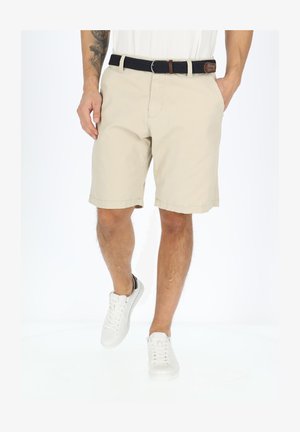 Beżowe szorty z gładkim przodem, tylnymi kieszeniami zapinanymi na guziki oraz plecionym czarnym paskiem. W połączeniu z białymi sneakersami z czarnymi akcentami.