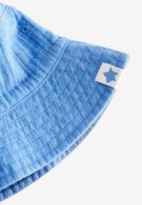 Hellblauer Bucket Hat aus strukturiertem Baumwollstoff, mit einem weißen Etikett mit einem blauen Sternakzent und gestickten Details entlang des Schirms.